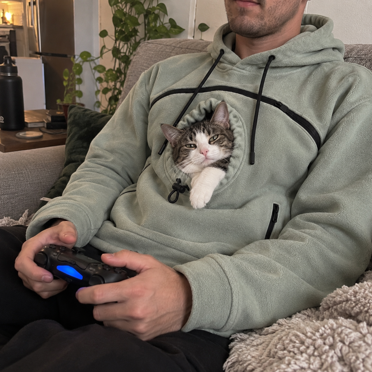 Seated person wearing a muted green hoodie with a cat